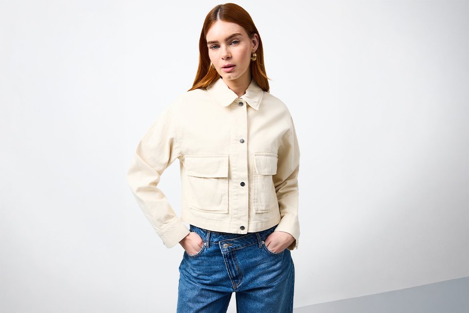 Cream cropped jacket layered over yellow shirt with blue jeans styled for UK staycation outfit.