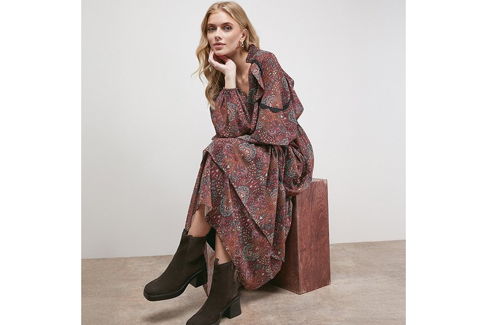 Woman wearing a floaty paisley dress, paired with brown boots.