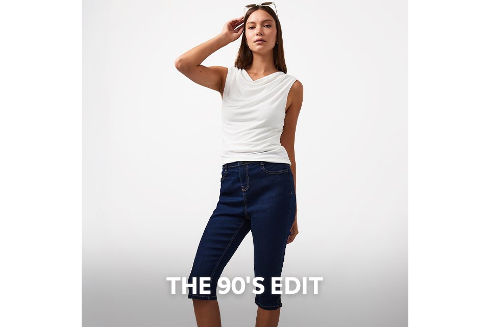 Woman wearing dark high rise capri jeans, paired with a white high neck sleeveless top.