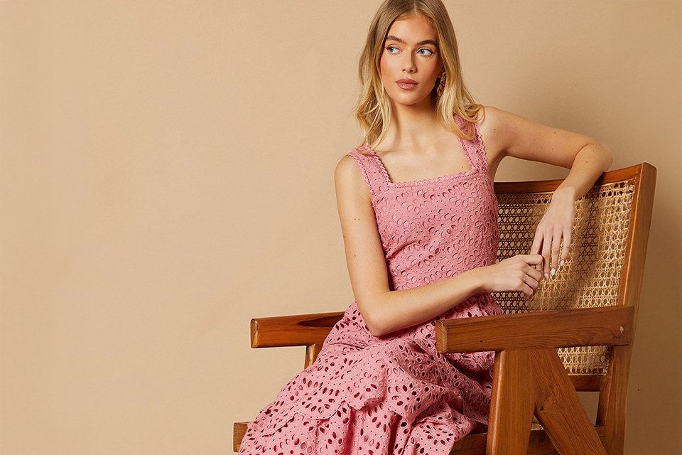 A woman sitting in a chair wearing a pink dress and brown block shoes.