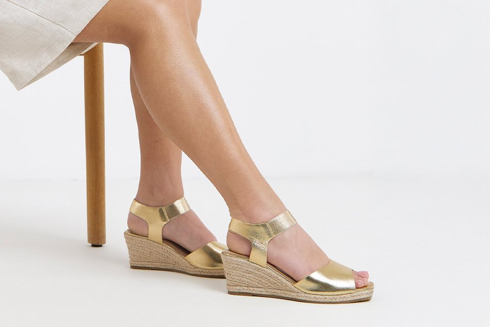 Woman sitting down showing her legs, with gold wedge shoes.