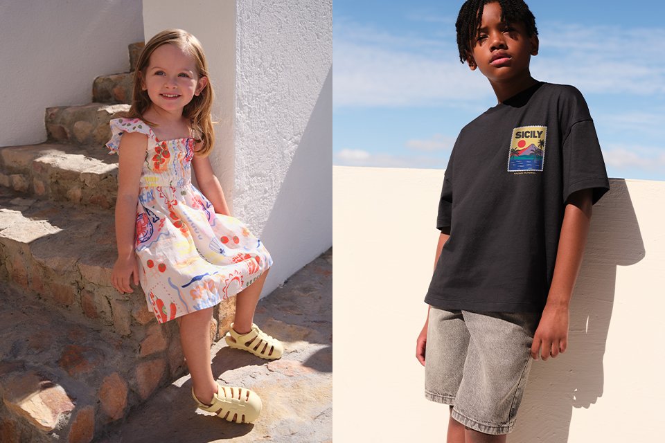 A picture showing two children, one child wearing a dress with graphic dress and yellow sandals, and the other wearing a black top with denim shorts.