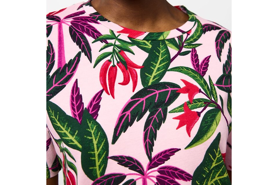 Pink floral print top featuring a vibrant tropical leaf and flower pattern in green, red and purple tones.
