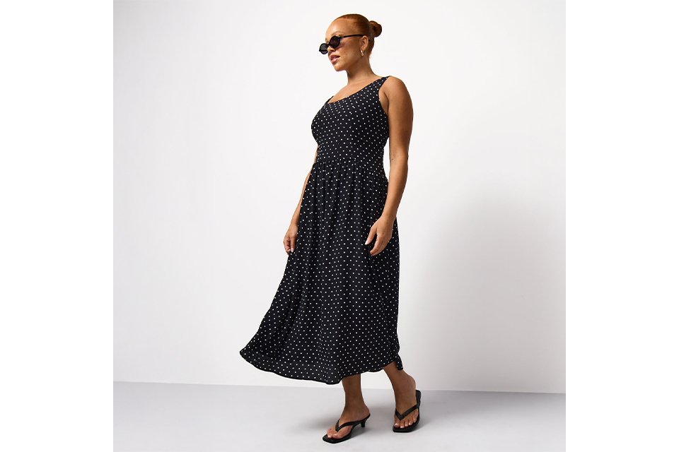 Black sleeveless midi dress with an all-over white polka dot print, featuring a fitted bodice and flowing skirt.