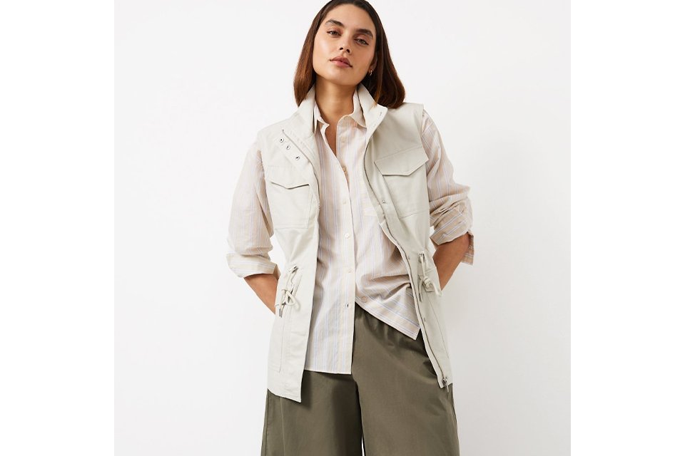 A woman wearing khaki balloon trousersm with a white shirt, and a neutral waistcoat.