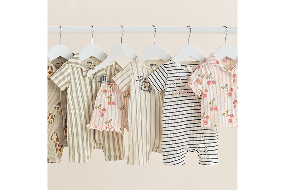 Baby clothing collection featuring striped rompers, animal print bodysuits, cherry print shorts and matching shirt sets hanging on a clothing rail.