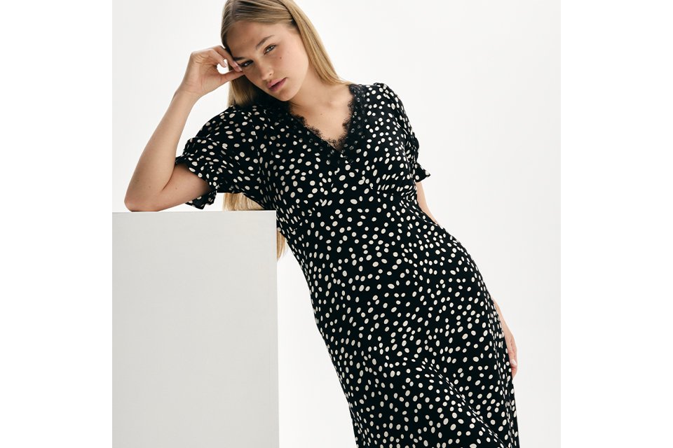 Black midi dress with white polka dot print and short ruffle sleeves, styled in a minimalist studio setting.