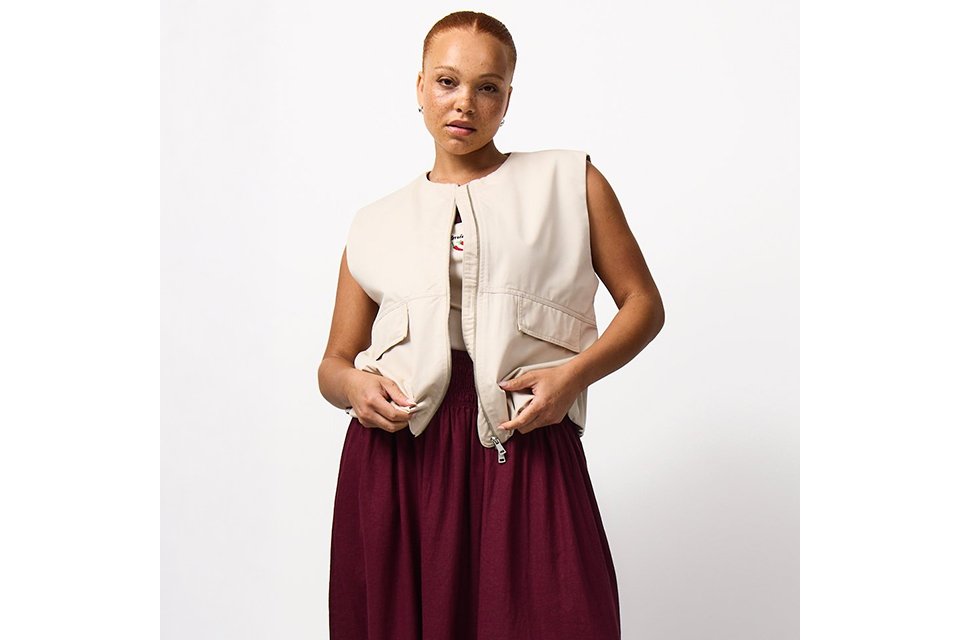 Burgundy maxi skirt styled with a cream sleeveless utility gilet featuring front flap pockets and a zip fastening for a contemporary casual look.