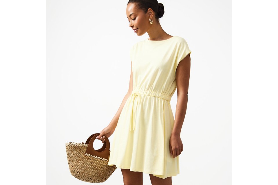 Light yellow sleeveless mini dress with a drawstring waist, relaxed fit and soft draped silhouette, styled with a woven straw handbag.