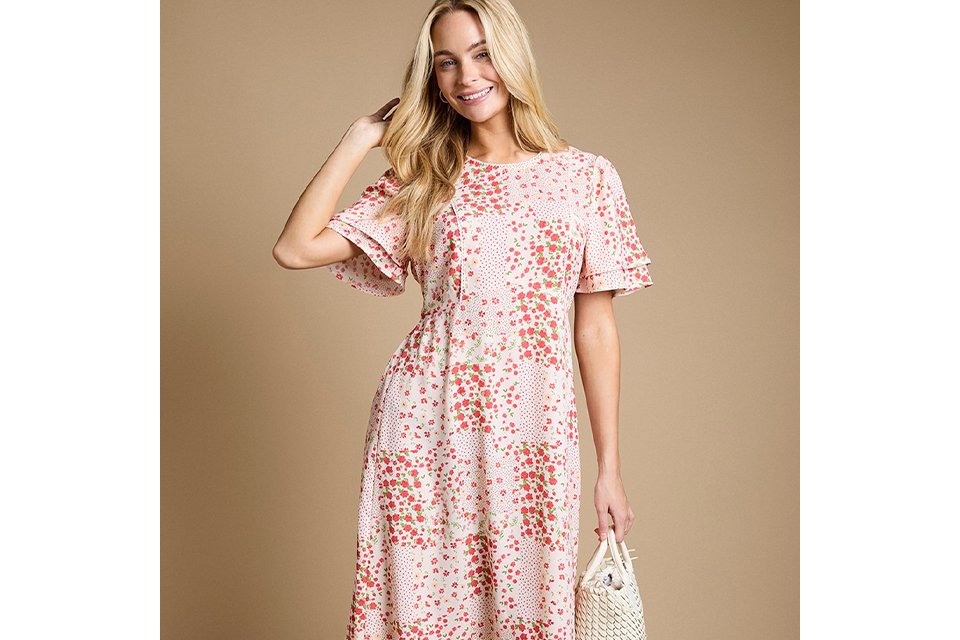 Blush pink floral print maxi dress with flutter sleeves, round neckline and flowing tiered silhouette, styled with a woven handbag.