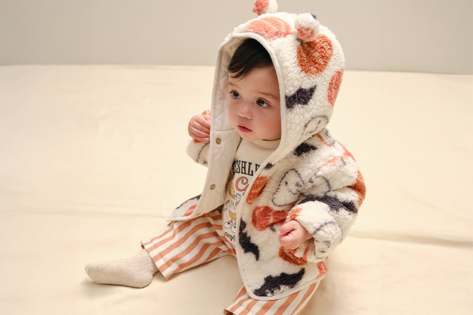 Baby Halloween outfit sets featuring pumpkin graphic sweatshirts, navy and cream harlequin trousers, and orange pumpkin-print leggings, displayed in a flat-lay clothing arrangement on a neutral background.