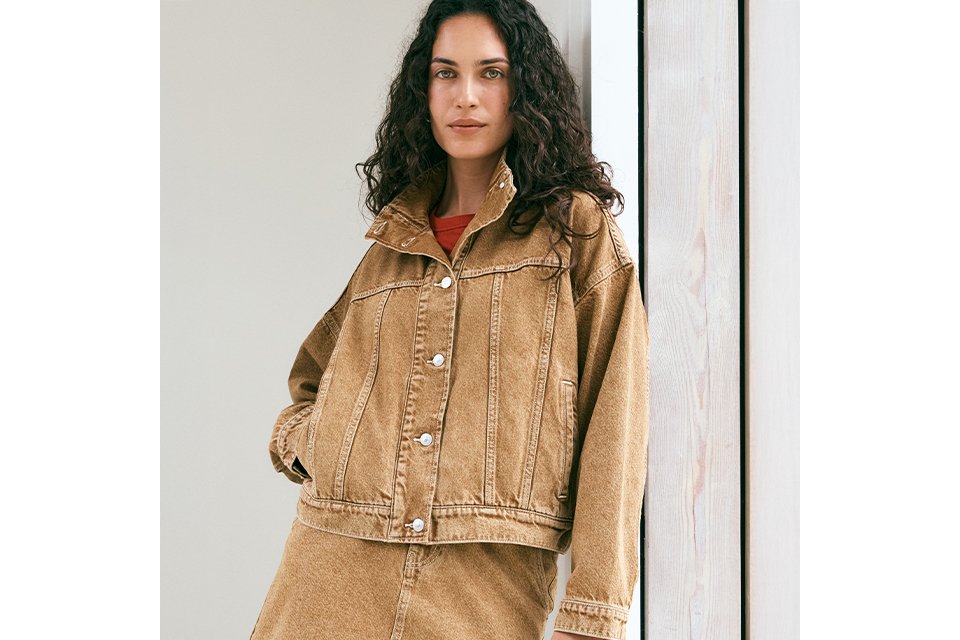 A woman wearing a tan denim co-ord with a denim jacket and a denim skirt.