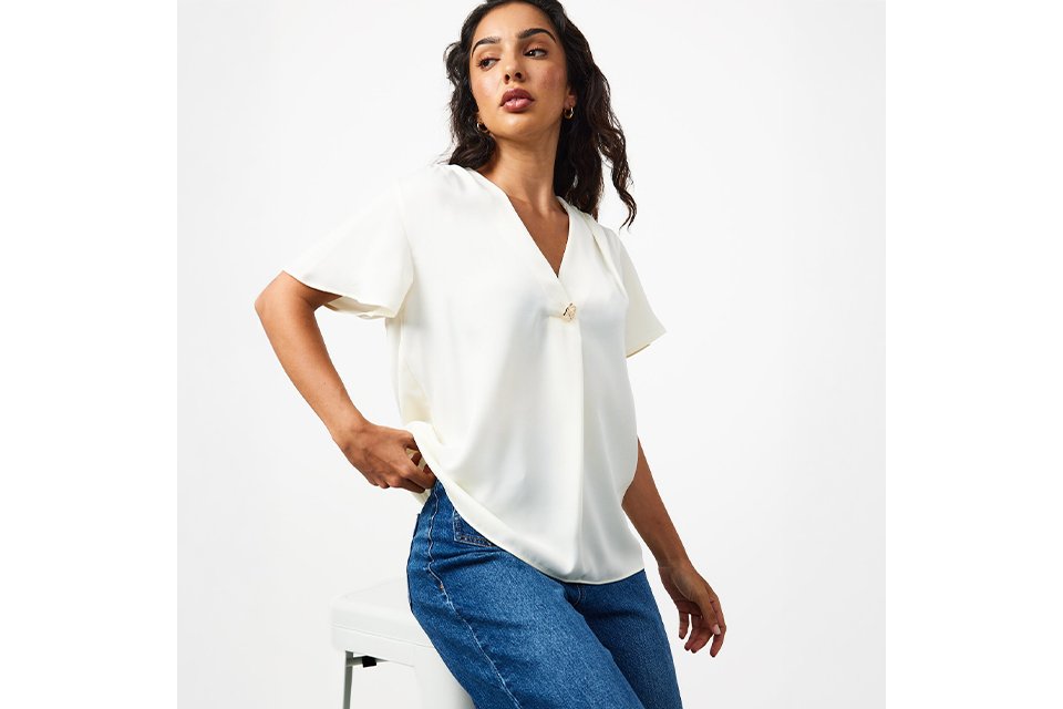 A woman wearing a cream top with blue jeans.