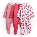 Three baby sleepsuits hanging on white hangers, including a red and white striped design, a plain pink design, and a white strawberry-print design with "Bon Appetit" text.