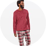 Person wearing a long-sleeve burgundy fleece top paired with red, black, and white plaid pyjama bottoms, sitting against a plain white background.