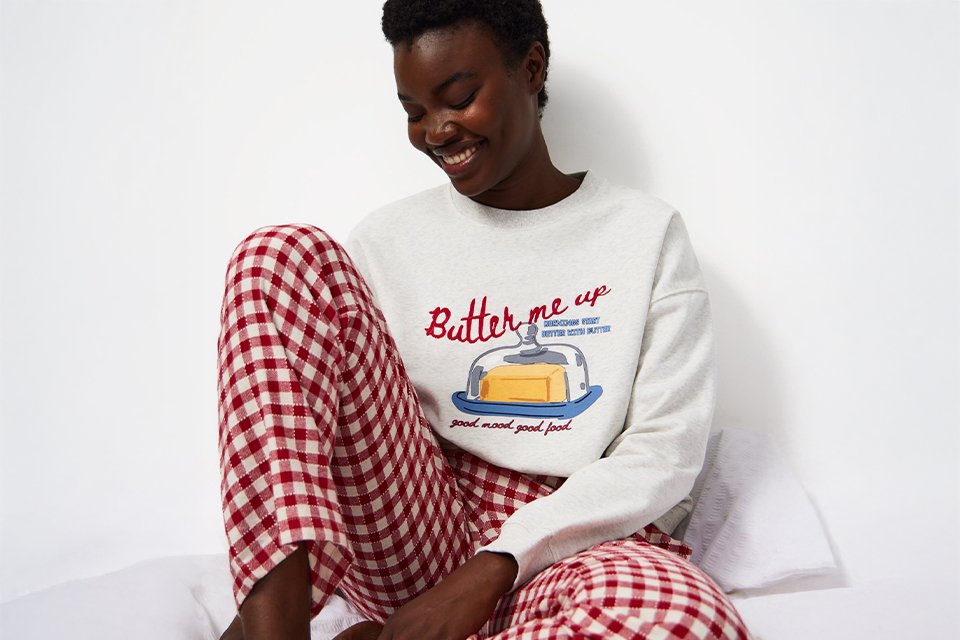 A woman wearing a pyjama set with red and cream gingham bottoms and a cream long sleeve pj top.