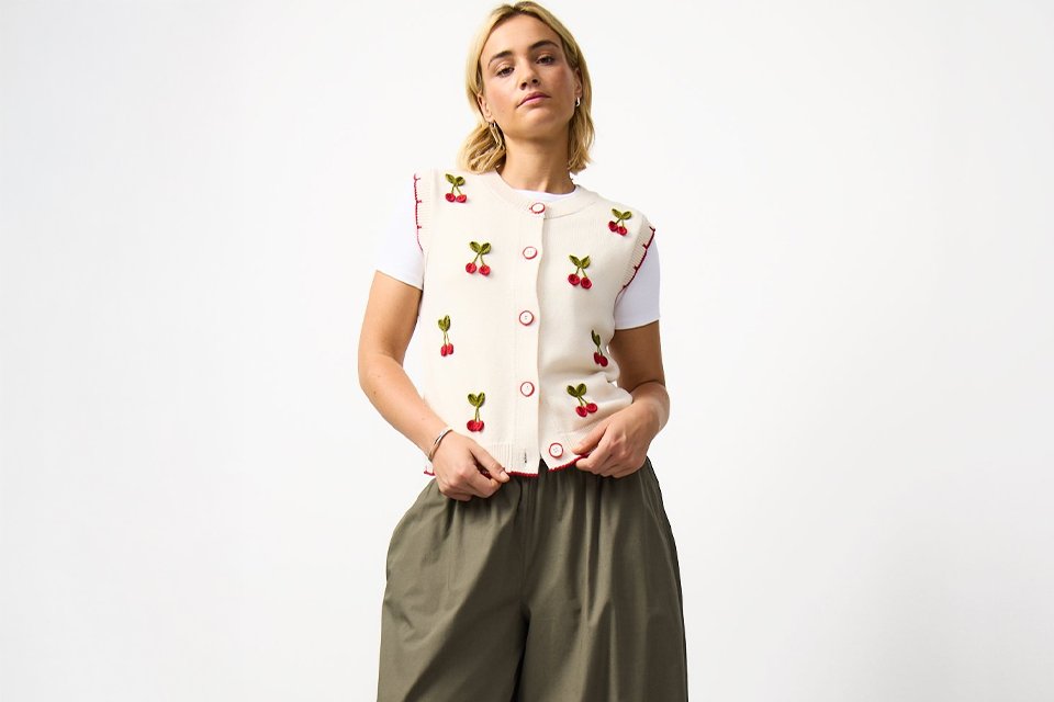 A woman wearing khaki balloon leg trousers, with a cherry print waistcoat.