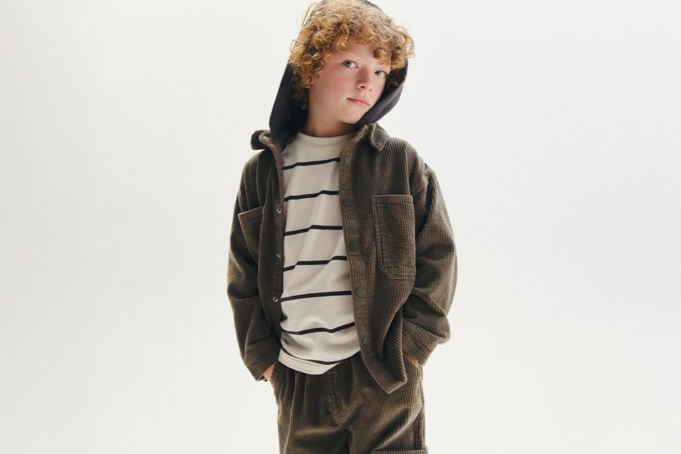 A boy wearing a corduroy co-ord, with a stripey top underneath.