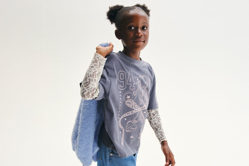 A girl wearing a long denim skirt, with a t-shirt, and long lace top underneath.