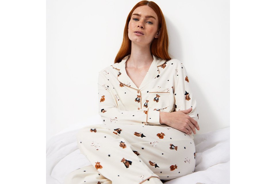 erson wearing white printed pyjamas sitting on a bed, featured in the Tu Clothing nightwear guide.
