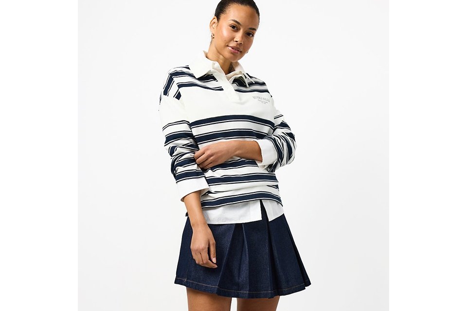 A woman wearing a stripey long-sleeve top, with a denim mini skirt, and loafers with socks.