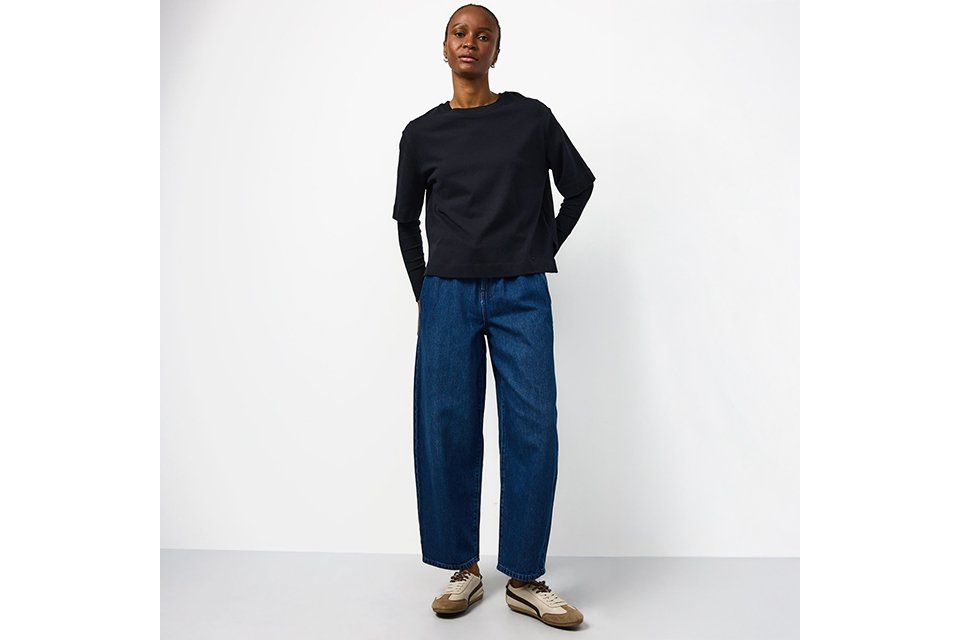 women wearing blue barrel leg jeans, with a black basic long sleeve top and trainers.