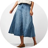 Light wash denim midi skirt with a flared silhouette, panel detailing, and a high-waisted fit, styled with a cream sleeveless top and ballet flats.