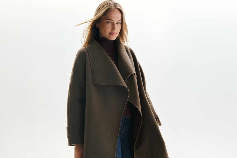 A woman wearing a roll neck jumper with jeans with a coat over the top.
