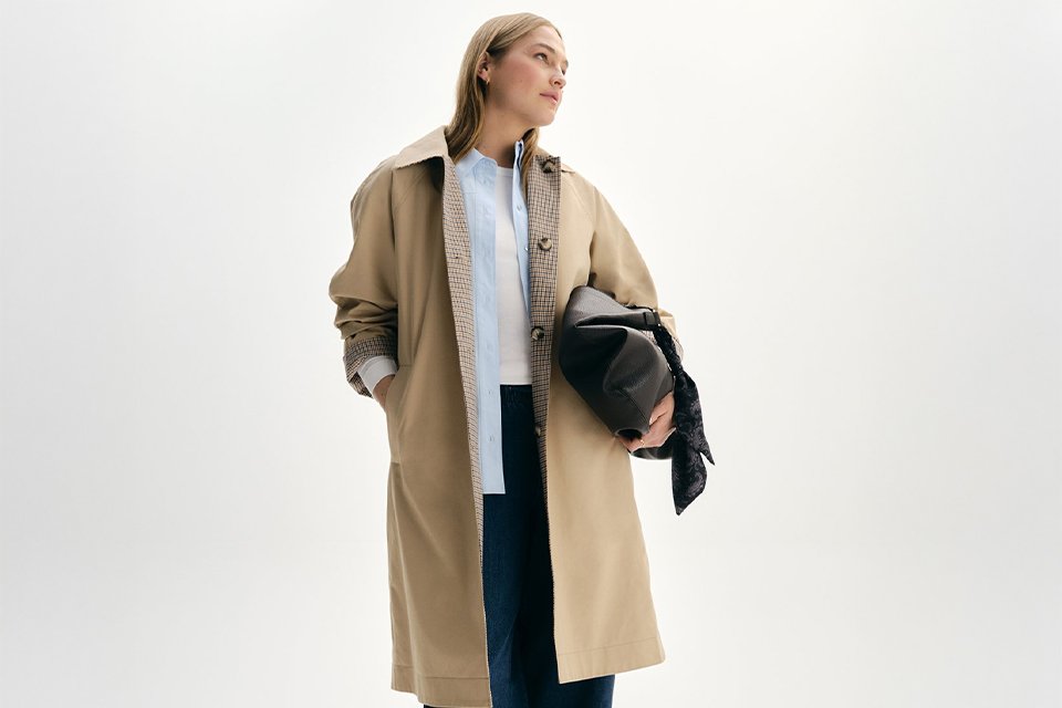 A woman wearing a white top with blue shirt, paired with barrel-leg trousers, and then a reversible trench coat.