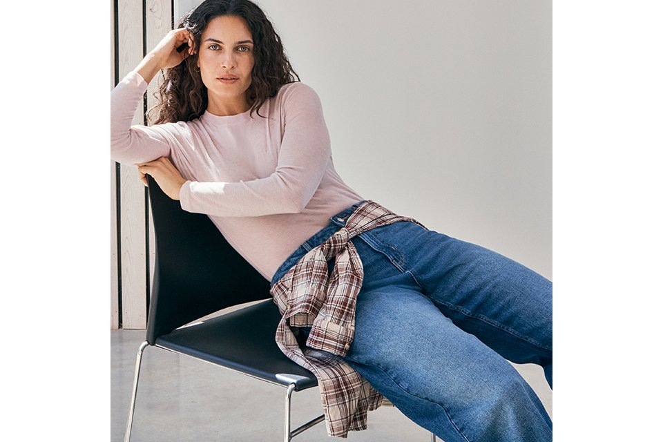 A woman wearing a basic long sleeve top with jeans,and a check shirt tied around her waist.