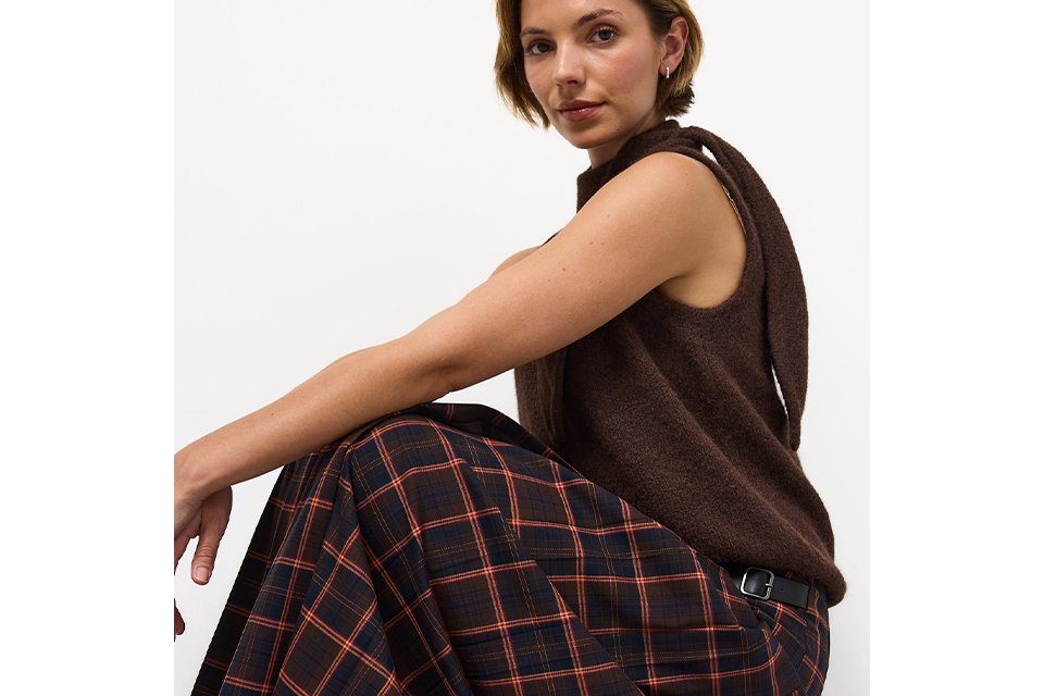 A woman wearing a check skirt and brown sleeveless top.