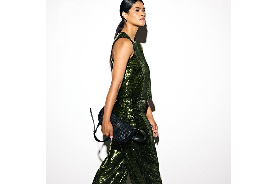 Side view of a person in a full-length green sequin dress holding a black handbag.