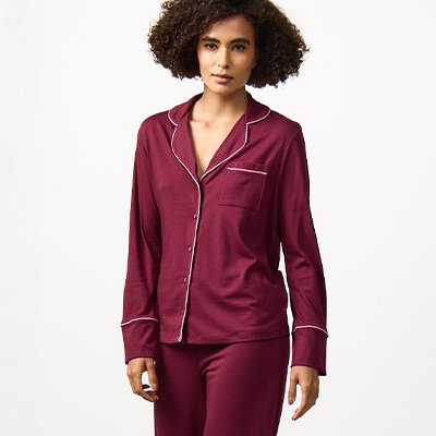 Women's satin pyjama set in burgundy with long-sleeve button-up top and matching trousers, comfortable coordinated nightwear.