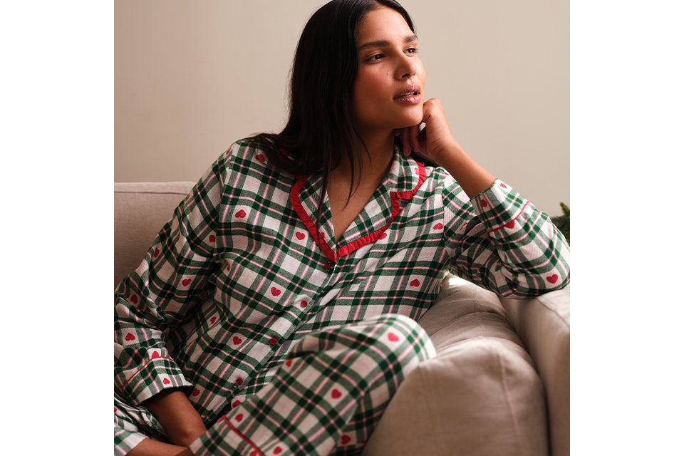 Person relaxing in traditional tartan check Christmas pyjamas with red and green festive styling.
