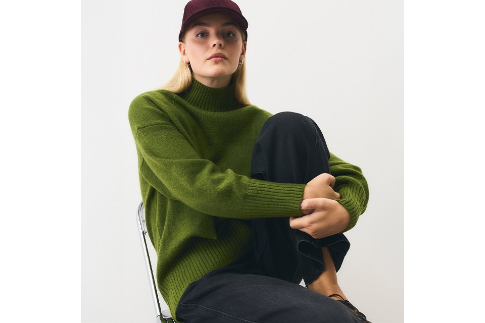 Close-up of a child wearing a brown graphic sweatshirt featuring playful dinosaur illustrations and bold cream lettering, photographed indoors against a neutral tiled background.