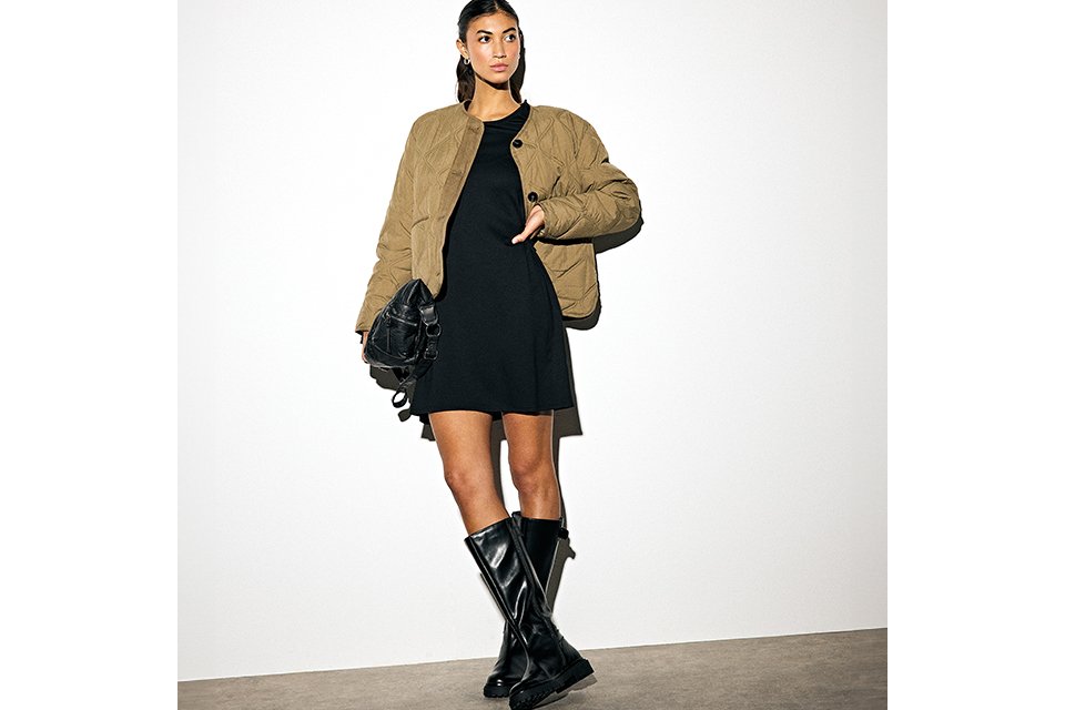 Casual outfit with black dress, bomber jacket, flat boots, and clutch bag.