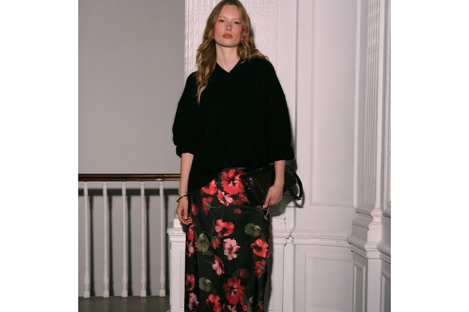 Women's black oversized knit sweater paired with a black floral midi skirt with red rose pattern and lace trim.