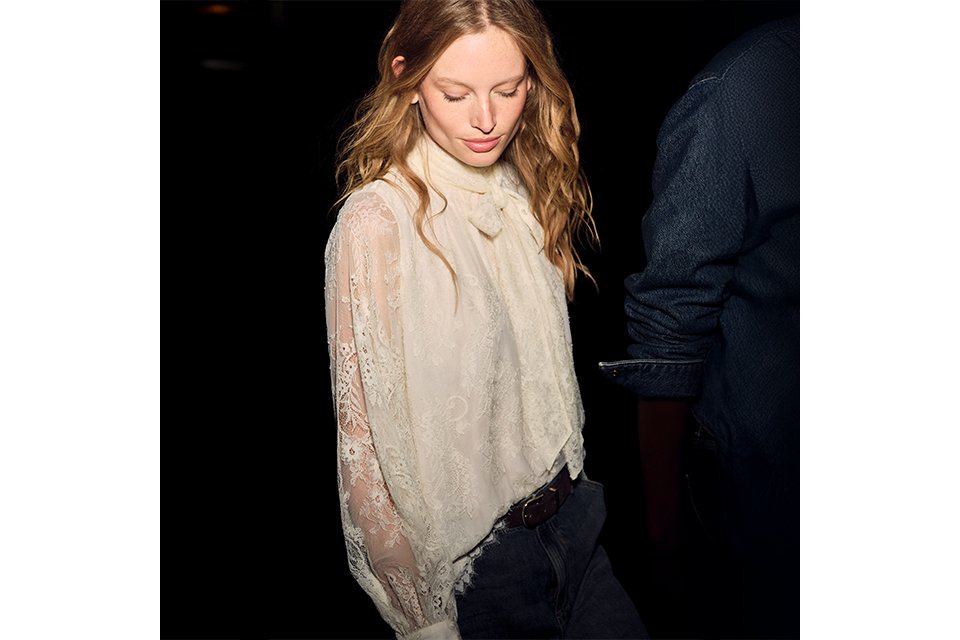 Cream lace high-neck blouse with tie-neck detail and sheer long sleeves, styled with blue denim jeans for an elegant casual outfit.