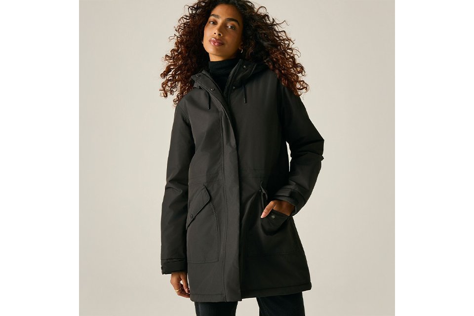 Black hooded waterproof parka jacket worn over a black turtleneck, featuring a full front zip closure, adjustable hood, and utility pockets in a minimalist studio setting.