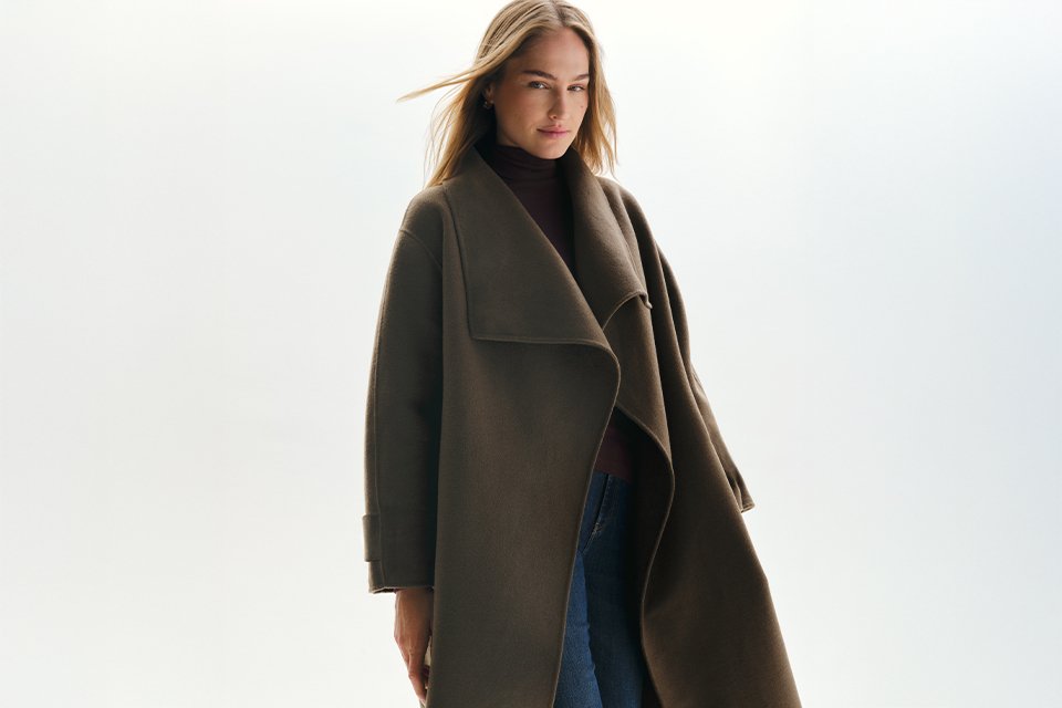 Long dark brown wrap coat with an oversized draped collar, layered over a dark turtleneck top and blue denim jeans for an elegant autumn and winter outerwear look.