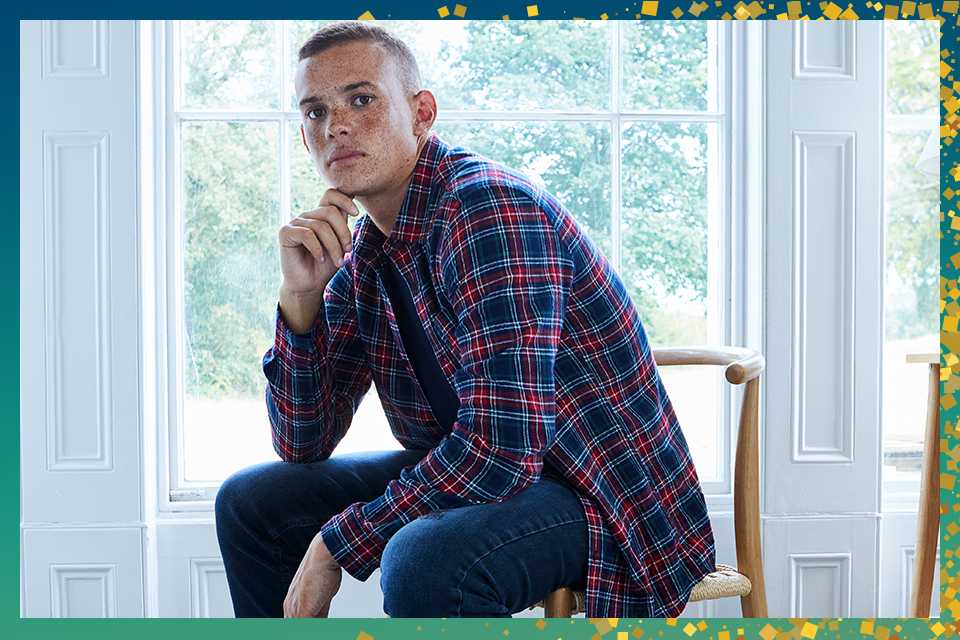 Man in checked shirt and jeans sitting on chair.