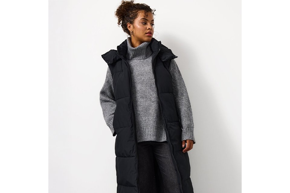 A woman wearing a grey jumper, with dark jeans and a black longline padded gilet.