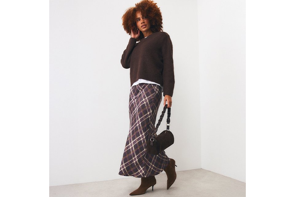 Woman wearing brown jumper and check midi skirt with brown kitten heeled boots.