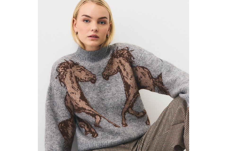 A woman wearing a grey jumper with brown horses on it.