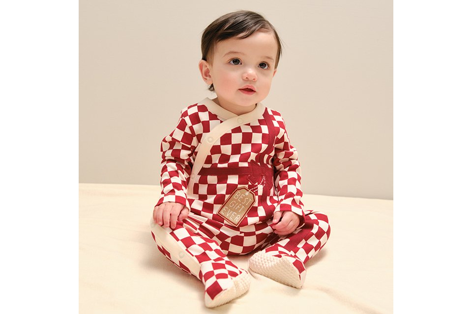 A baby wearing a red and white checkered sleepsuit with a 'best gift ever' motif.