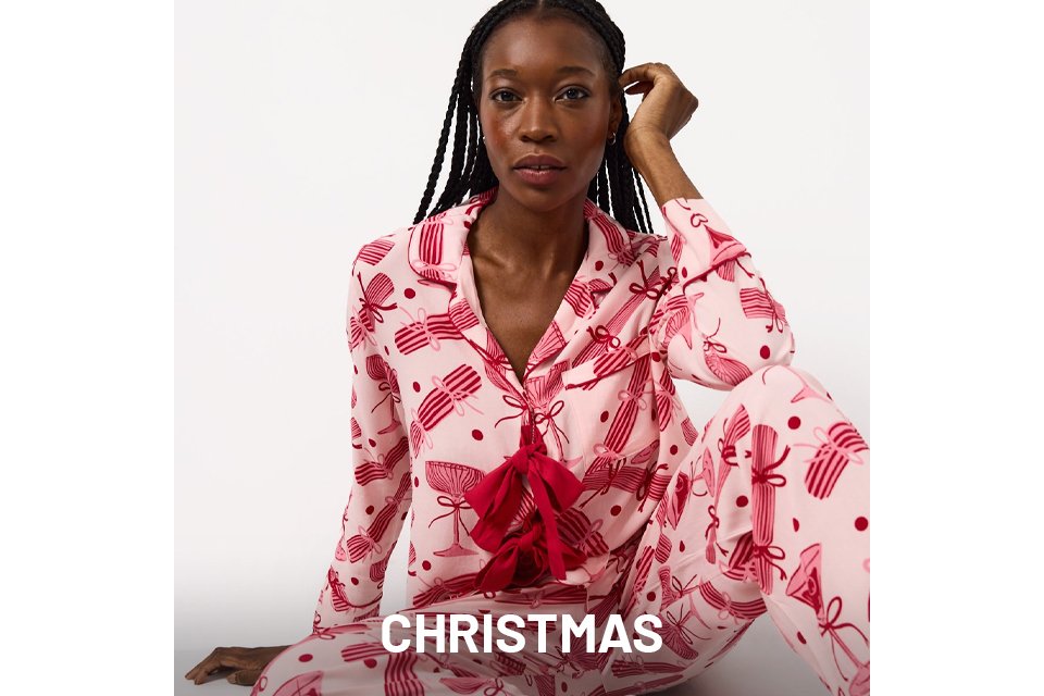 Person wearing pink pajamas with red bow patterns, sitting cross-legged on a white background.