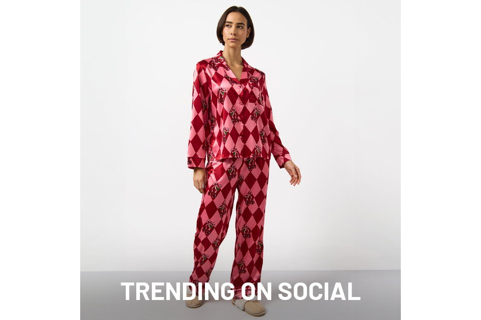 Person wearing a pink and red satin pajama set with a diamond pattern and decorative motifs, paired with beige slippers, standing against a plain white background.