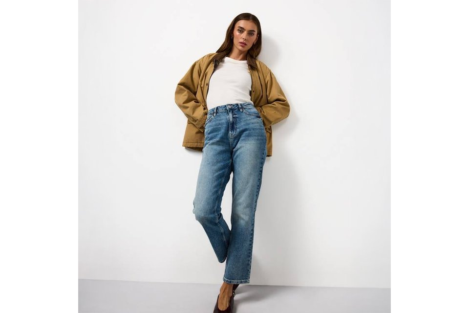 Woman wearing straight leg jeans a white t shirt and tan jacket.