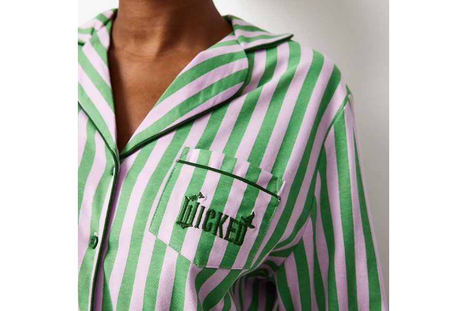 Woman wearing green and pink stripe pyjama top, with wicked embroidered on the pocket.