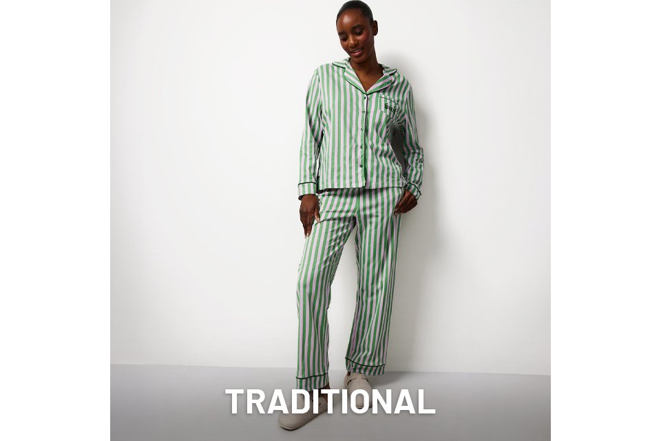 Person standing against a white background wearing a green and white vertically striped pajama set with a button-up top and matching pants, paired with light-colored slippers.